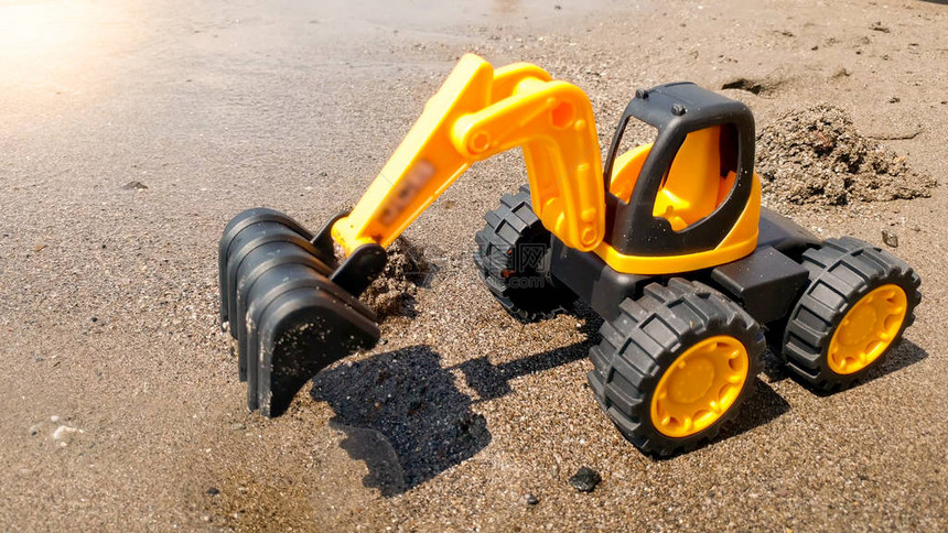 玩具挖掘机在海滩上挖湿沙子的近距离图像图片