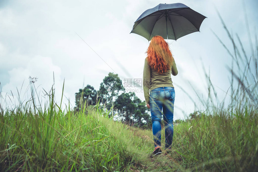 妇女在雨季在绿草地上站着伞子图片