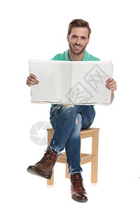 身着绿色马球衬衫双腿穿白色背景阅读报纸的年轻图片