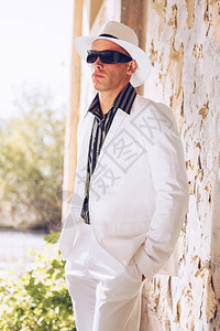 戴着黑色太阳镜白色帽子和白色夏季西装摆姿势的时髦男人图片