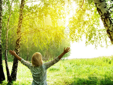女人在树林附近的森林里开阔地向阳光举起双手图片