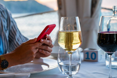 晚餐时女人的手拿着智能手机精美的餐桌与地中海餐厅桌上的酒杯假日晚餐在图片