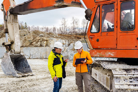 戴头盔的男女工人或地质学家在采石场建筑设备的背图片