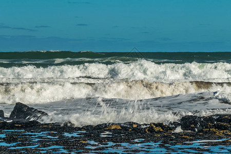 海浪拍打着海岸附近的石头白色泡沫从海浪中涌出蓝天海图片