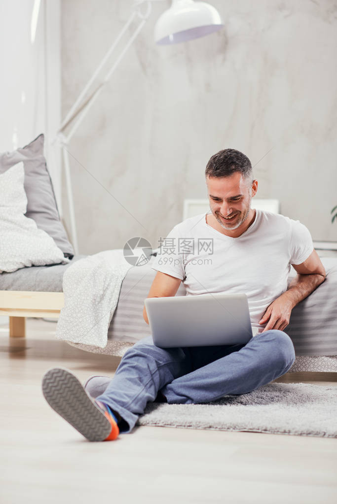 英俊的中年男子坐在地板上靠在床上并图片