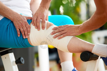 近身受膝盖疼痛折磨的妇女在健身房有绷带腿的无脸妇女锻炼期间肌肉紧张医图片