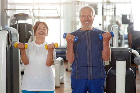 微笑的高级夫妇在健身房的画像快乐的老男人和女人拿着哑图片