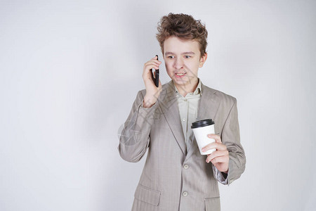 身穿灰色商务服带着手机和纸杯咖啡站在白色工作室背景的年轻少图片