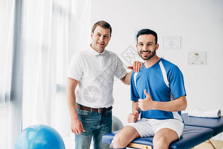 微笑着的生理治疗师在快乐的足球运动员面前露出大图片