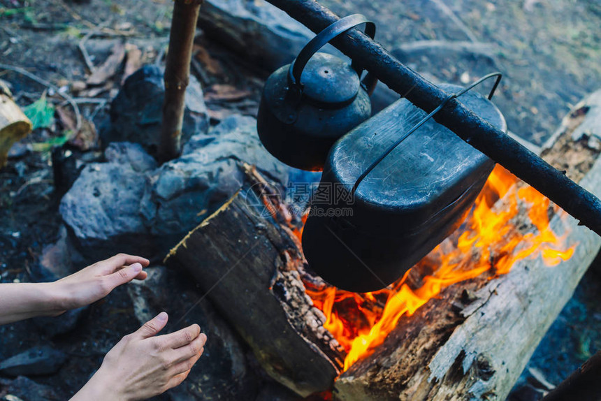 露营时用火暖手篝火上方的大锅和水壶在大自然中烹饪食物户外晚餐木柴和树枝着火在森图片