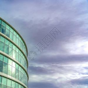 一座现代办公大楼的正方形外观有反射玻璃墙在楼上可以看到满是灰色云彩图片