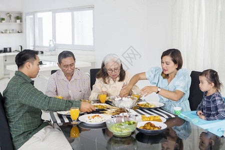 年轻女在家共进晚餐时为大家庭提供食物的图片