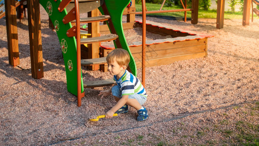 3岁蹒跚学步的小男孩坐在操场上用玩具塑料铲挖沙子的肖像图片