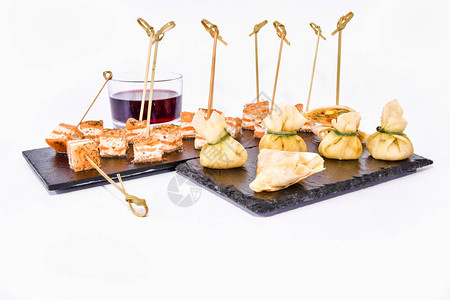 三文鱼串配奶酪饺子和黑盘子上的红酒图片