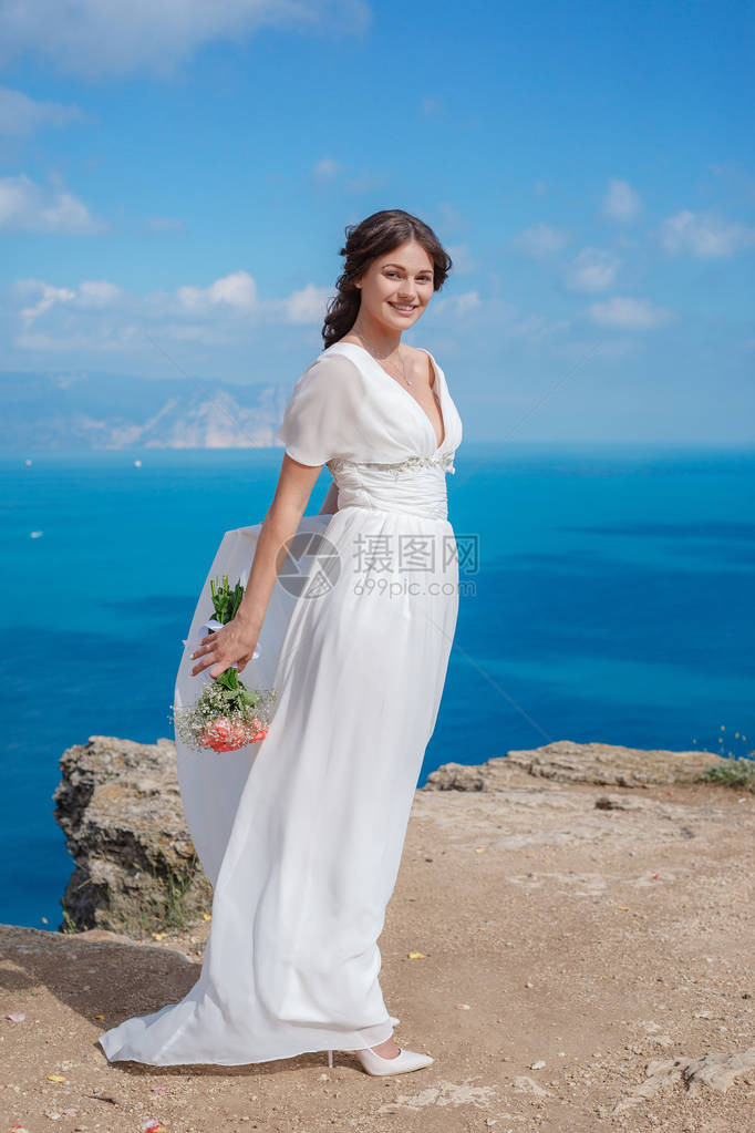 美丽的新娘站在海边山中的新娘婚礼摆在背景海的白色礼服的浪图片