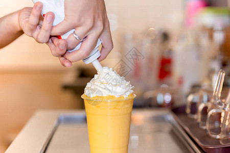手在橙色冰沙饮料杯上挤奶油图片