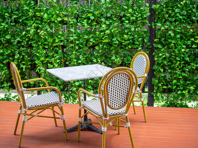 三把木制白色复古椅子与白色大理石桌子在绿色常春藤植物背景的红色地板上图片