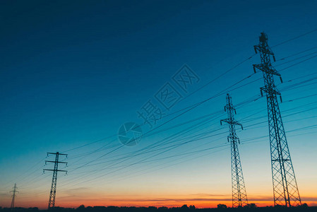 日出背景场中的电源线黎明时分电线杆的剪影温暖的橙色蓝天上的高压电缆夕阳下的电力行业在如诗画的生动天空背景图片
