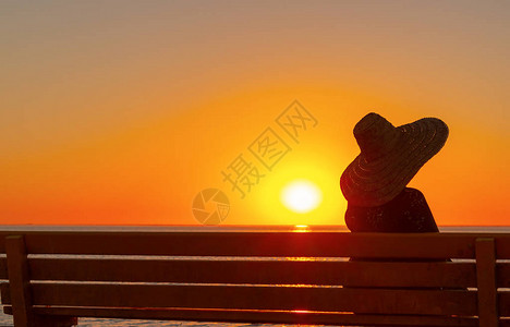 戴大帽子的女人坐在长凳上看日落图片