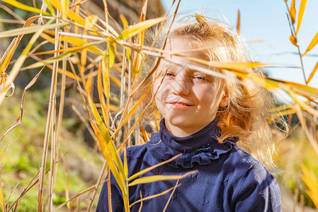一位身穿蓝色毛衣的美丽年轻女孩在河岸的芦苇丛中微笑图片