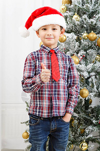 男孩在圣诞节树附近戴着圣诞帽图片