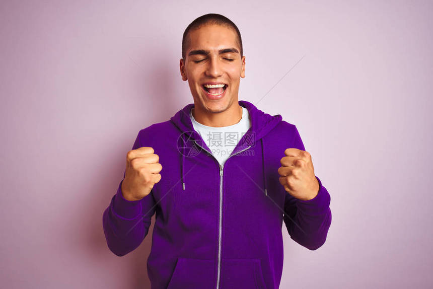 年轻英俊的男人在粉红色的孤立背景上穿着紫色运动衫图片