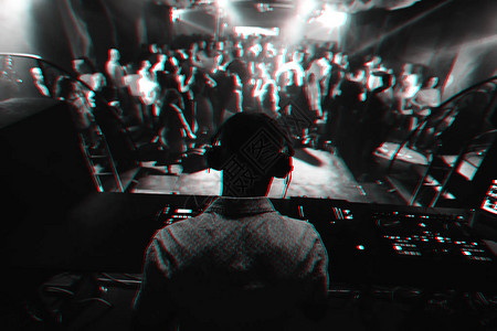 在搅拌机上播放音乐的DJ影集和很多人在舞台上的夜总会里跳舞图片