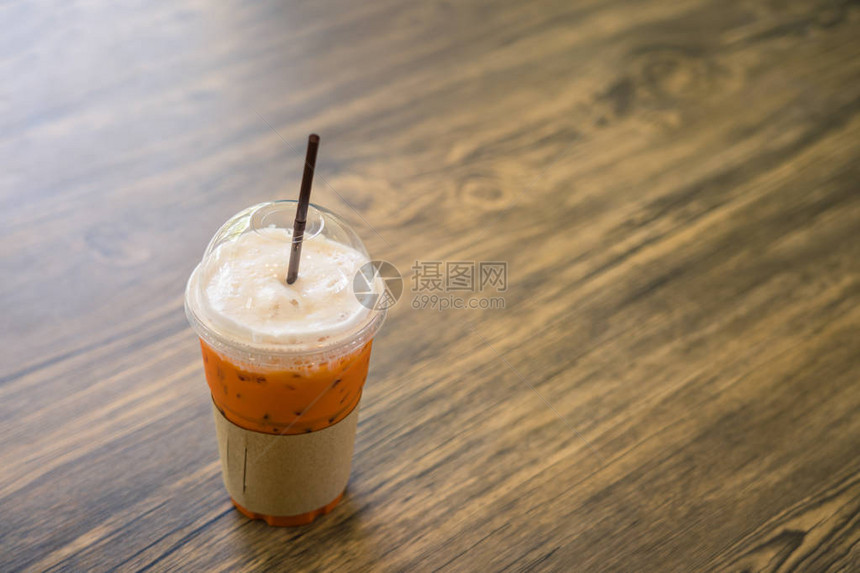 在咖啡馆的木桌上的泰国冰茶塑料杯图片