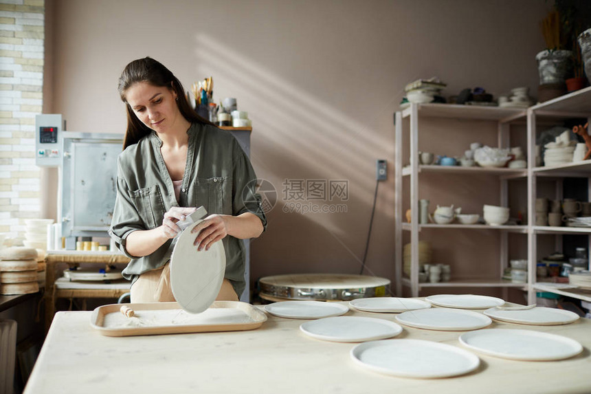 年轻女子在陶艺车间打磨手工陶瓷板的腰部肖图片