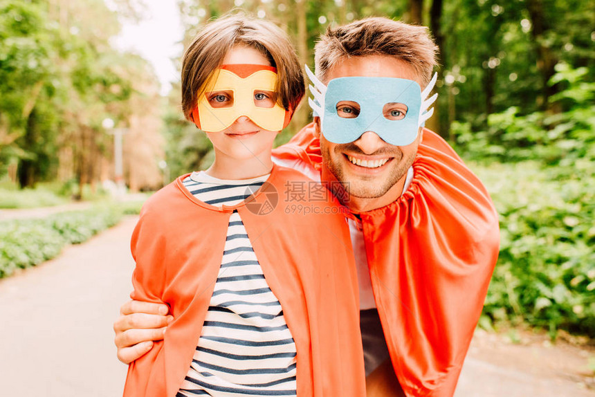 快乐的父亲和儿子站在红色斗篷和超级英雄面具上图片