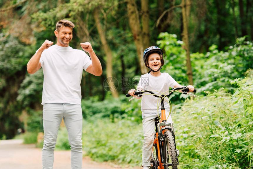 父亲微笑着为儿子欢呼而男孩则骑着自行图片