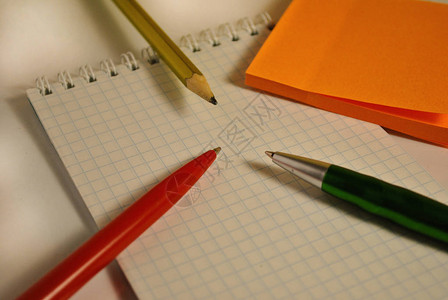 记事本背景上的橙色贴纸钢笔和铅笔图片