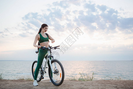 日出时骑自行车后背着包检查脉搏的美丽年轻黑发女子的画像模特早上用无图片