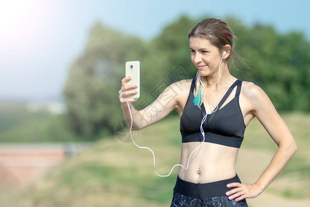 健身运动感女孩在锻炼休息期间在智能手机上制作自拍照片背景中的城图片