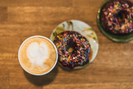 邓肯森糟糕的早餐咖啡店里的木桌上有一颗心和牛奶的咖啡咖啡旁边的桌子上散落着两个巧克力甜背景
