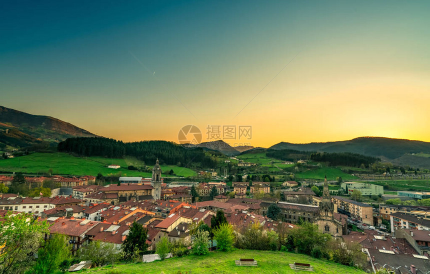 山谷中的城市与早晨的阳光黄色和蓝色的早晨阳光天空在山上欧洲的春季山上乡村的绿草场和松树林图片