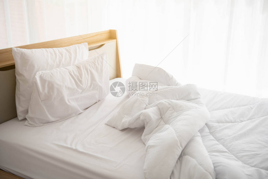 早晨的白色未整理床与阳光与白色窗帘背景在优雅的家室内设计和豪华家具概念室内生活方式和懒图片