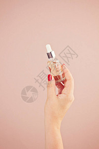 女手握血清皮肤护理产品在粉色糊面背景上反年龄美容护理福利图片