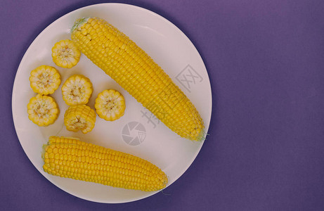 玉米在紫色背景上的盘子玉米切片谷物图片