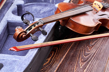 木制背景上的复古小提琴天鹅绒盒附近的旧老式小提琴和小提琴棒管图片