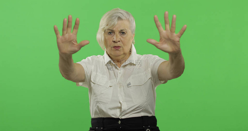 一位老妇人做了一个停止的手势一件白衬衫的老俏丽的祖母放置您的徽标或文本色度图片