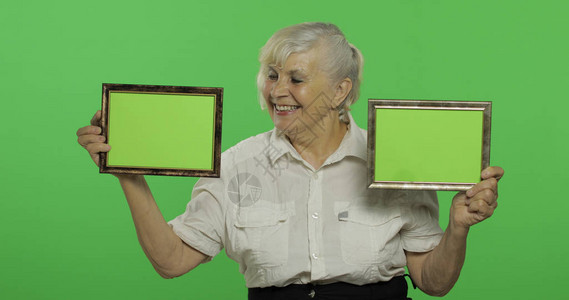 一位老妇人拿着两帧绿色图像一件白衬衫的老俏丽的祖母放置您的徽标或文本色度键绿屏背景背景图片