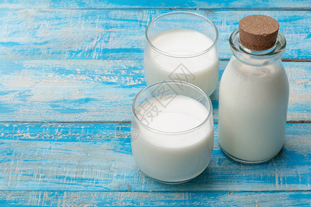 蓝色木桌上的一瓶牛奶和一杯牛奶健康图片