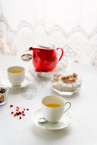 红色茶壶两个白色茶杯一个白桌上的糖碗图片