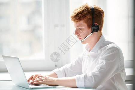 年轻呼叫中心接线员在办公室膝上型电脑前与在线客户通信背景图片