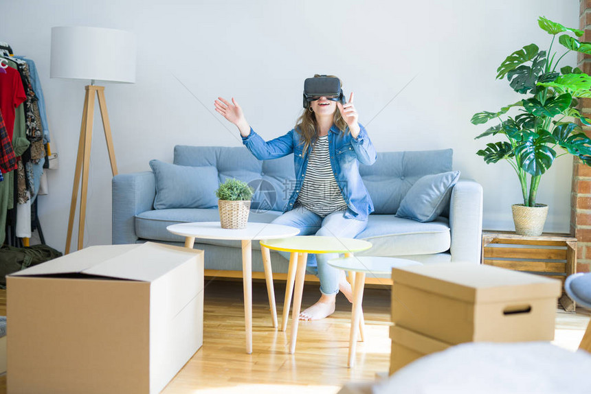 戴着虚拟现实眼镜的金发女郎坐在沙发上玩模拟游戏图片