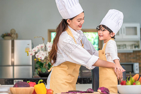 快乐美丽的亚洲女人打扮可爱的小男孩厨师装图片