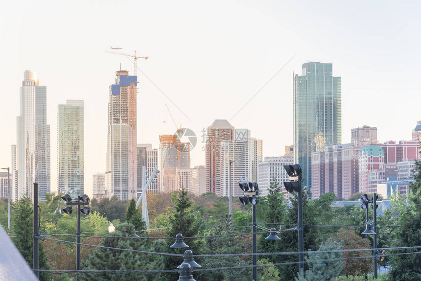 芝加哥密集的摩天大楼的查找视图与在建的新建筑和工作的起重机从有树和灯柱的城市公园在日落时向上看市图片