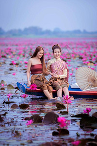 美丽的泰式女孩在红莲花池中快乐地坐在船上背景图片
