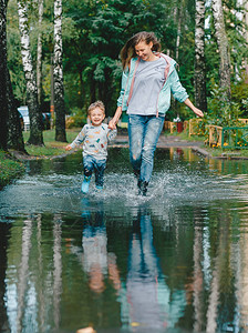 孩子和他的母亲在雨后的水坑上行走夏季阴雨天气概念家庭幸福的概图片